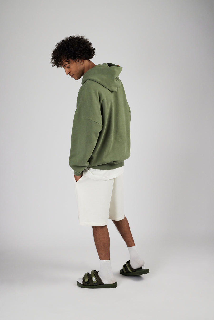 Backside view of a man wearing sweatshorts in color eggnog and oversized hoodie in color sage green