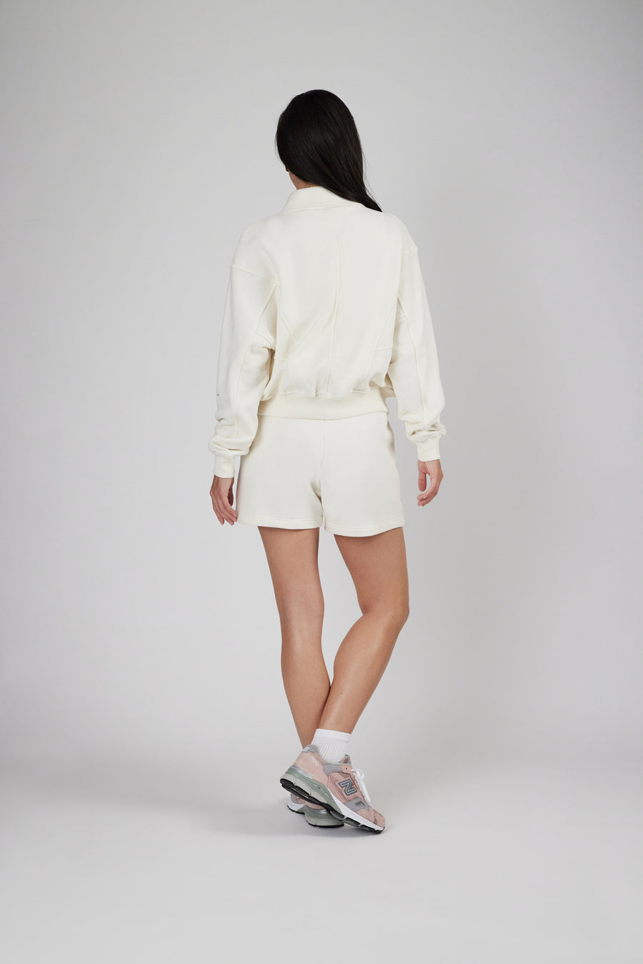 Backside view of a woman wearing a zipper sweat jacket and sweat shorts in color eggnog