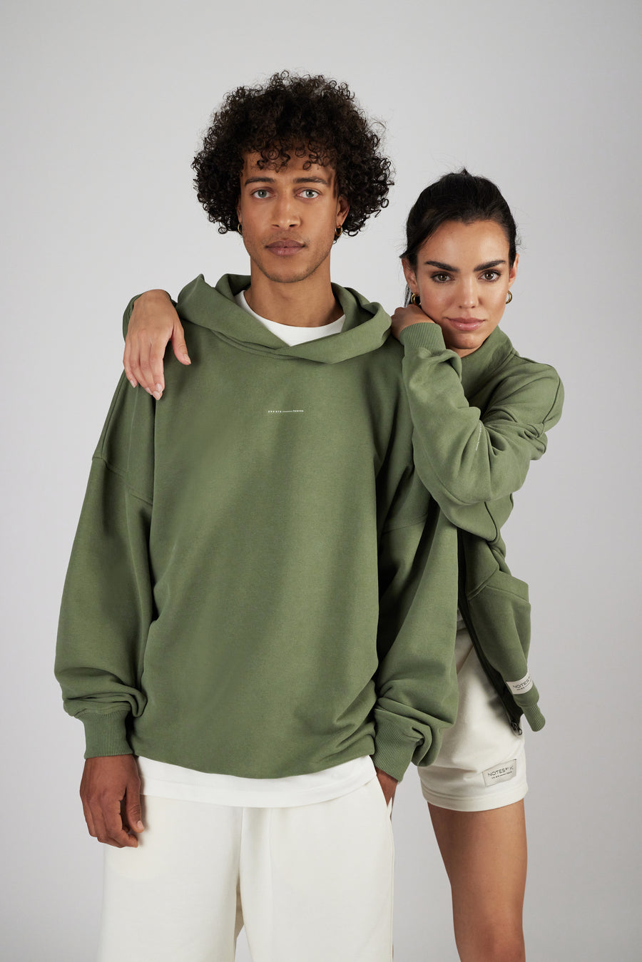 Men and woman wearing hoodie in sage green and shorts in offwhite