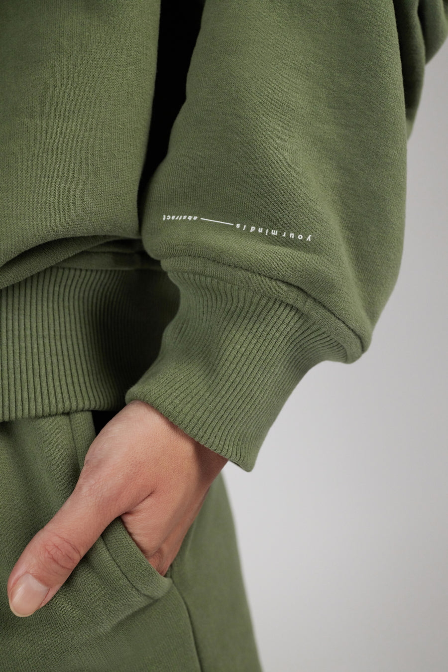 Hoodie in color sage green showing a small wording detail at sleeve