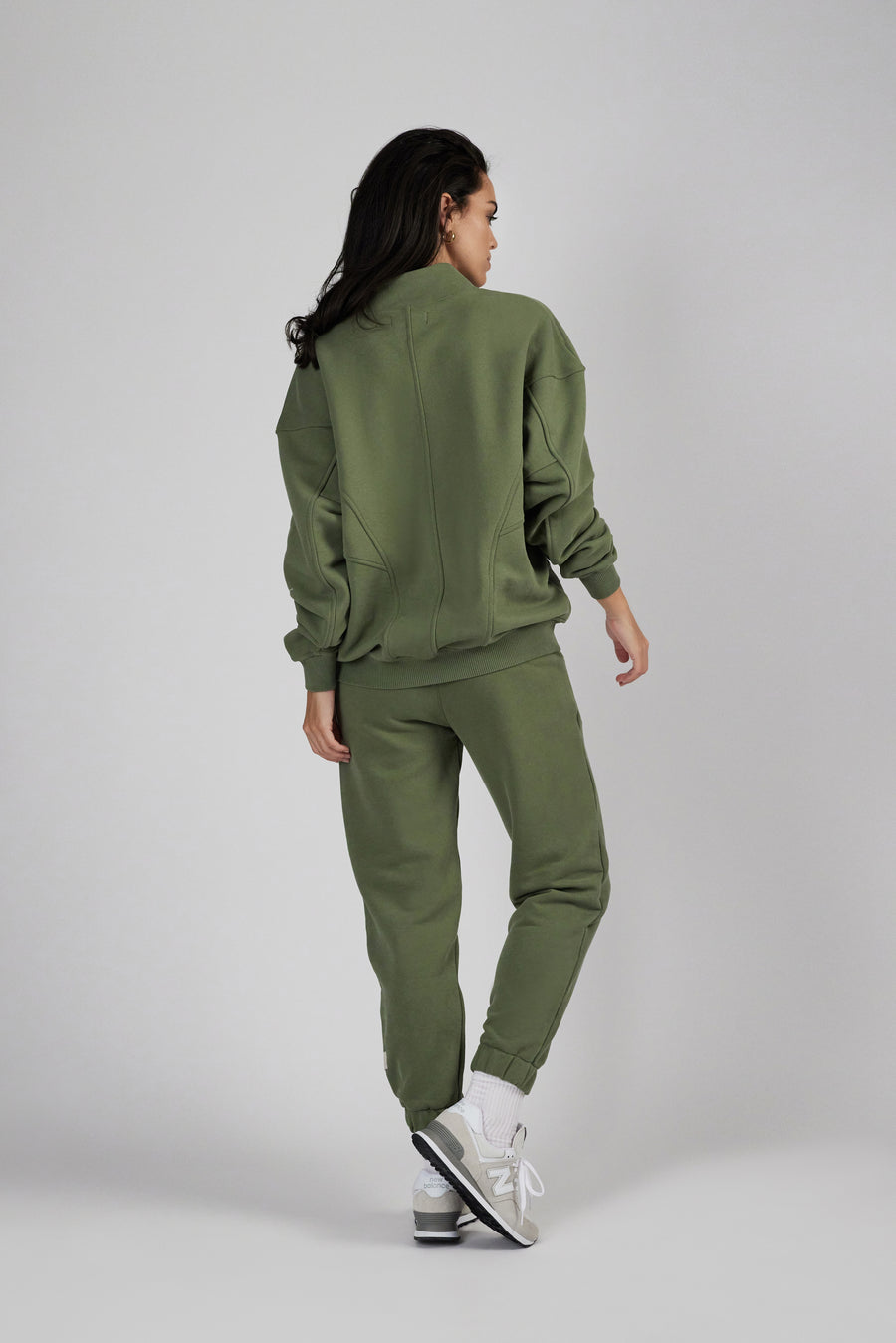 Backside of a woman wearing an oversized zipper sweat jacket and sweatpants in color sage green